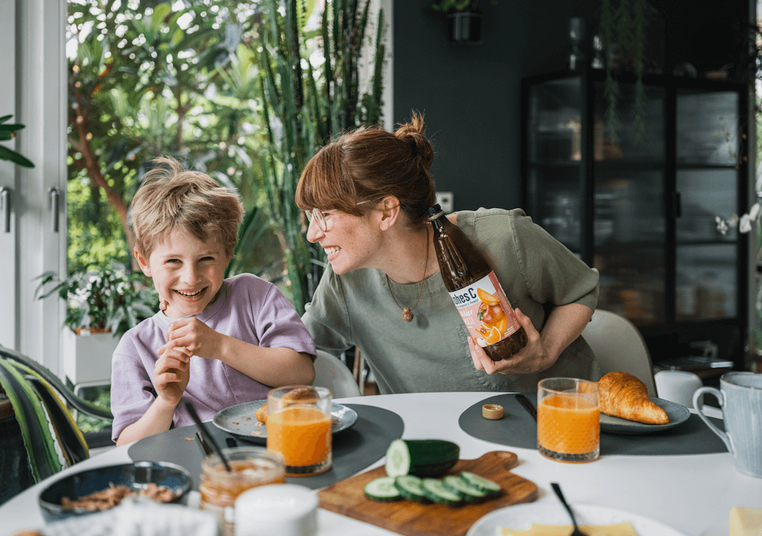 Eine Frau und ihr Sohn sitzen gemeinsam lachend am Frühstückstisch wo sie etwas essen und trinken, unter anderem hohes C, für die Eckes-Granini Success Story