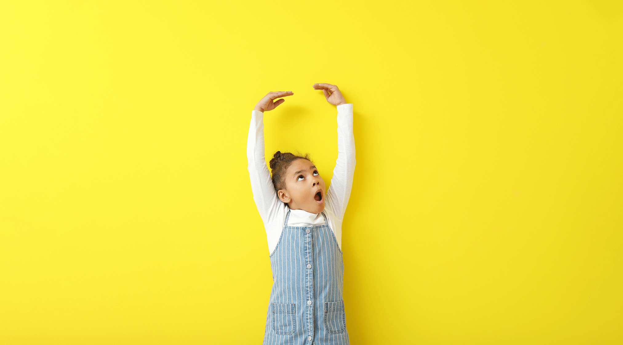 Little girl in front of a yellow background, showing how tall she will become one day