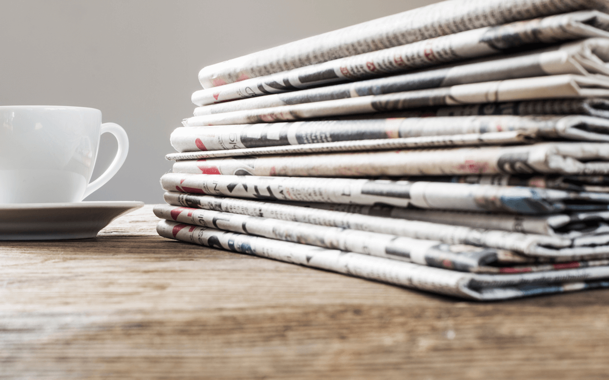 Ein Stapel Publikationen, wie Zeitungen oder Presse-Artikel sowie eine Tasse Kaffee auf einem Holztisch