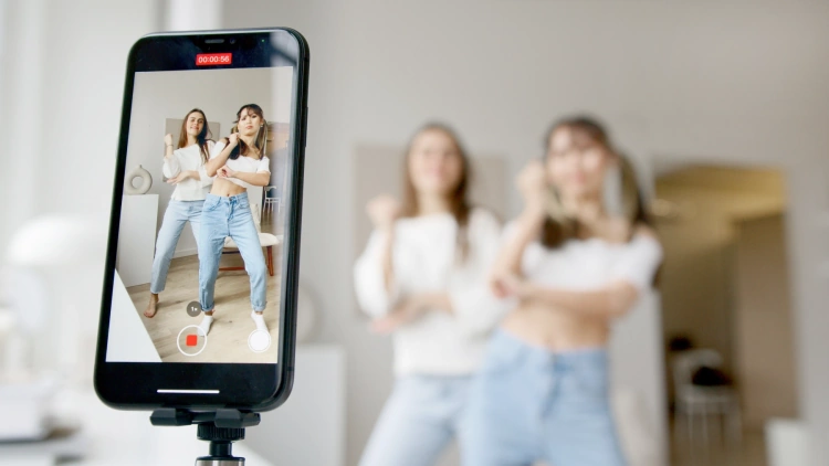 Zwei Influencerinnen tanzend vor einer Kamera eines Mobiltelefons, das ein Video von ihnen macht