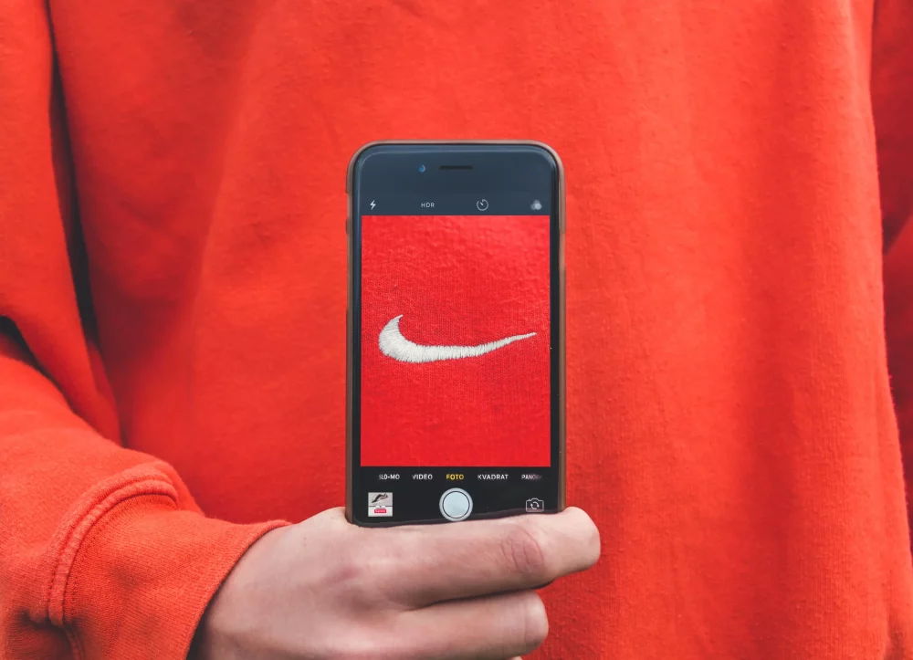 A Nike logo on a mobile phone held by a hand in front of a person with a red pullover